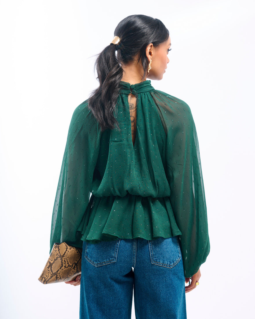 Woman wearing a green blouse with a sheer back and blue jeans, holding a clutch.