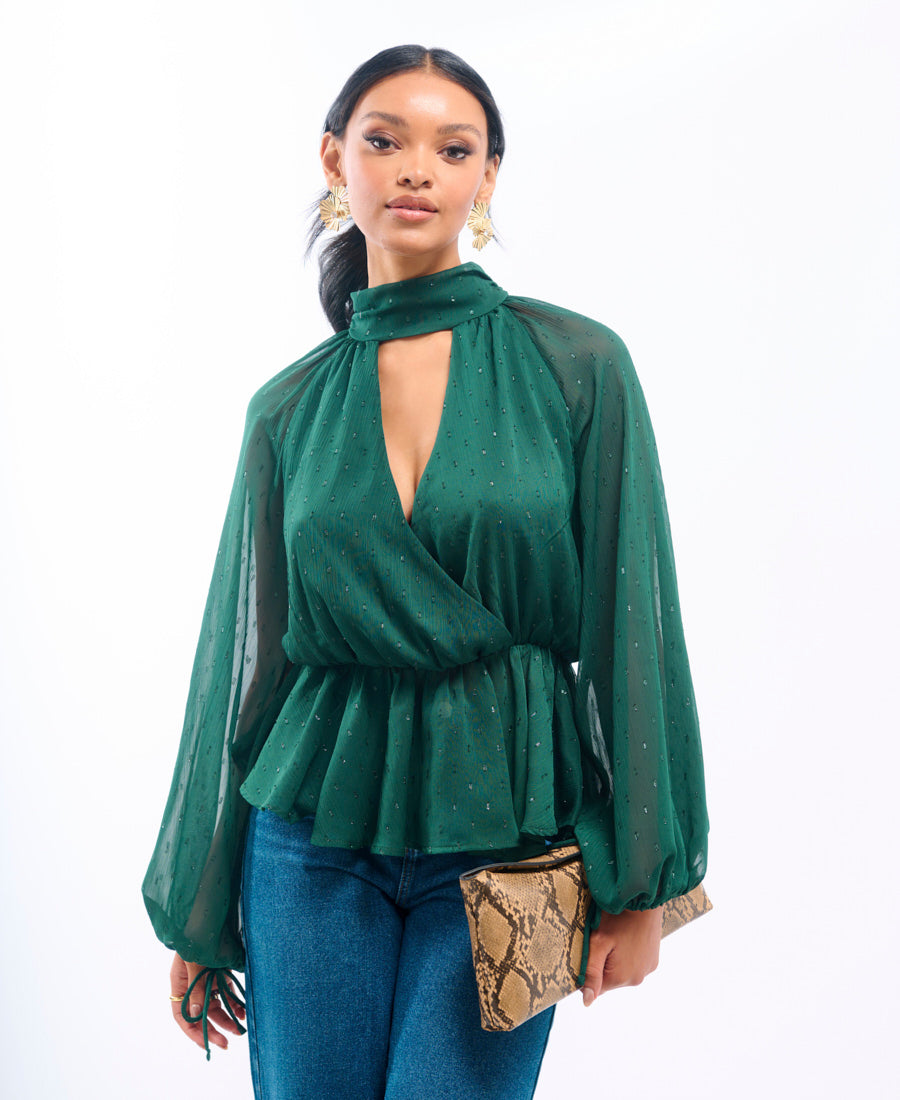Woman wearing a green blouse with sheer sleeves and cut-out design, holding a snake skin clutch.