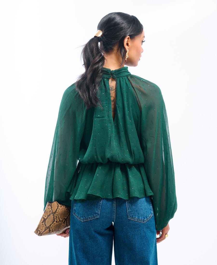 Woman wearing a green blouse with a sheer back and blue jeans, holding a clutch.