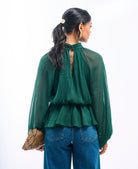 Woman wearing a green blouse with a sheer back and blue jeans, holding a clutch.
